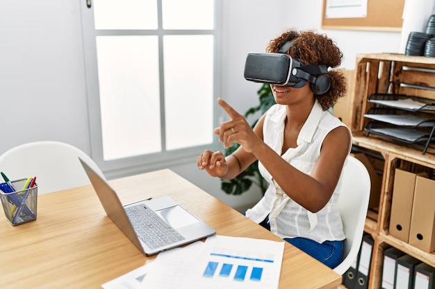 Joven afroamericana usando gafas de realidad virtual trabajando en la oficina