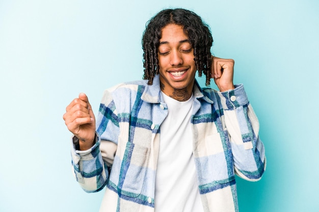 Joven afroamericano aislado de fondo azul bailando y divirtiéndose