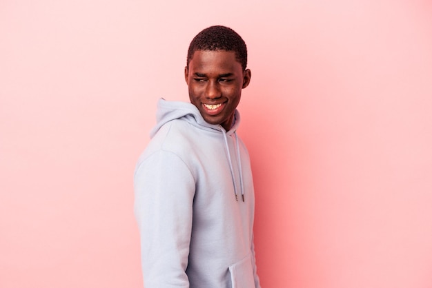 Un joven afroamericano aislado de fondo rosa parece sonriente, alegre y agradable.