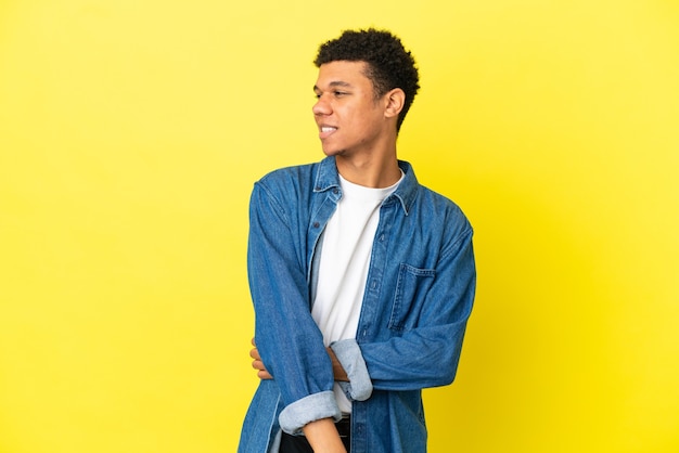 Joven afroamericano aislado sobre fondo amarillo mirando hacia el lado y sonriendo