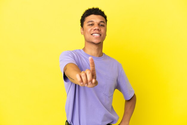 Joven afroamericano aislado sobre fondo amarillo mostrando y levantando un dedo