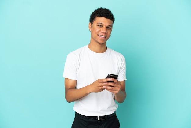 Joven afroamericano aislado sobre fondo azul enviando un mensaje con el móvil