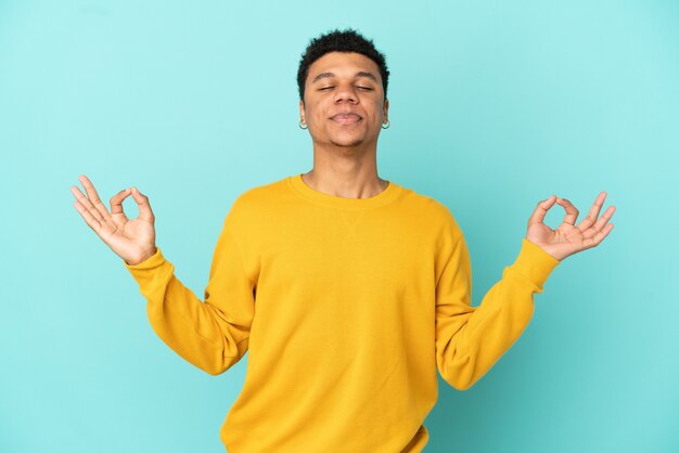 Joven afroamericano aislado sobre fondo azul en pose zen