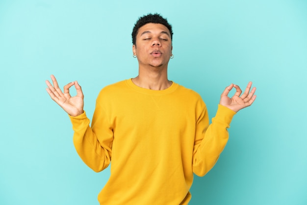 Joven afroamericano aislado sobre fondo azul en pose zen