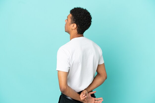 Joven afroamericano aislado sobre fondo azul en posición trasera y mirando hacia atrás