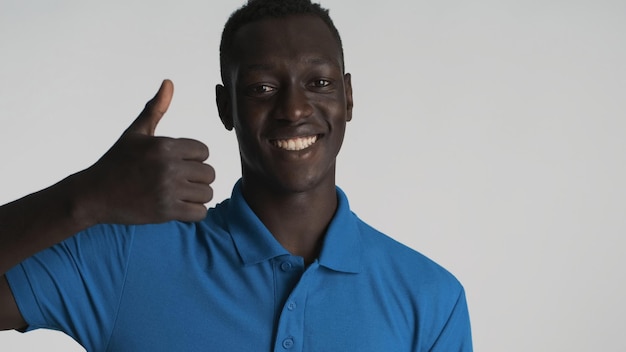 Joven afroamericano alegre mostrando el pulgar hacia arriba y sonriendo sobre fondo blanco Como signo