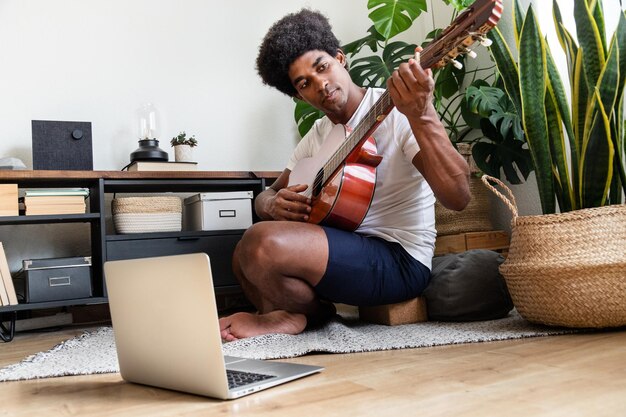 Joven afroamericano aprende a tocar la guitarra en casa con un curso en línea usando una computadora portátil