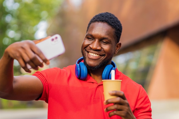 Joven afroamericano con auriculares en el cuello usando un teléfono inteligente en el parque de verano