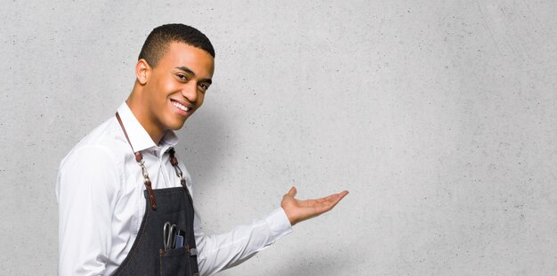 Joven afroamericano barbero apuntando hacia atrás y presentando un producto en la pared con textura