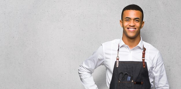 Joven afroamericano barbero hombre posando con los brazos en la cadera y sonriendo