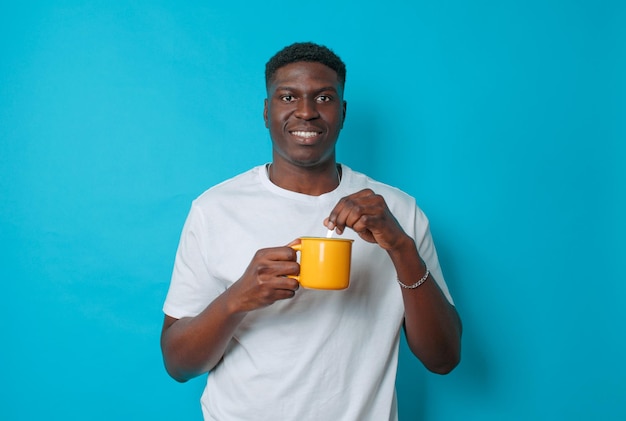 Un joven afroamericano bebe café de una taza amarilla revolviendo con una cuchara