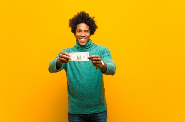 Joven afroamericano con billetes de un dólar contra la espalda naranja