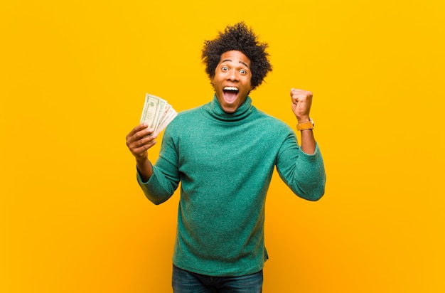 Joven afroamericano con billetes de un dólar contra la espalda naranja