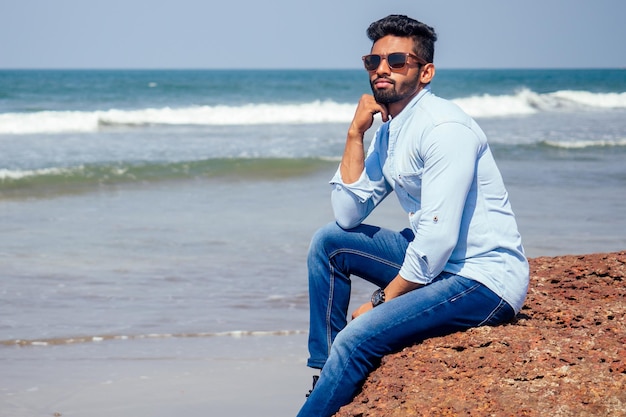 Joven afroamericano con camisa azul y jeans en la playa del océano.