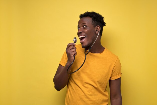 Joven afroamericano cantando con estetoscopio escuchando sus voces