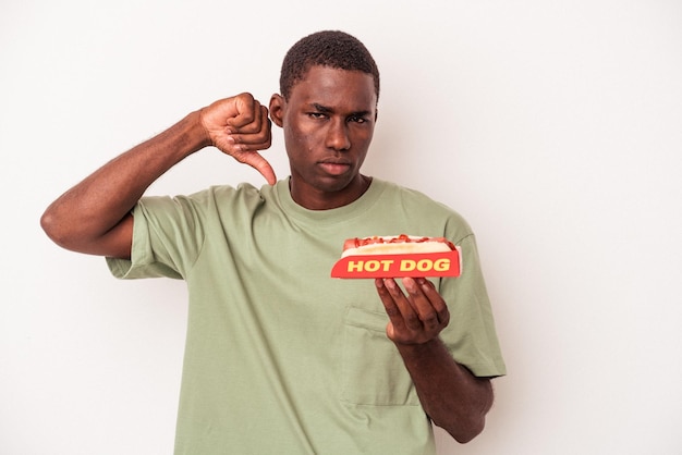 Joven afroamericano comiendo un perro caliente aislado de fondo blanco mostrando un gesto de disgusto, con el pulgar hacia abajo. Concepto de desacuerdo.