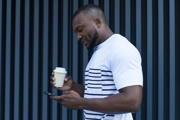 Un joven afroamericano elegante con un café y un teléfono inteligente en las manos