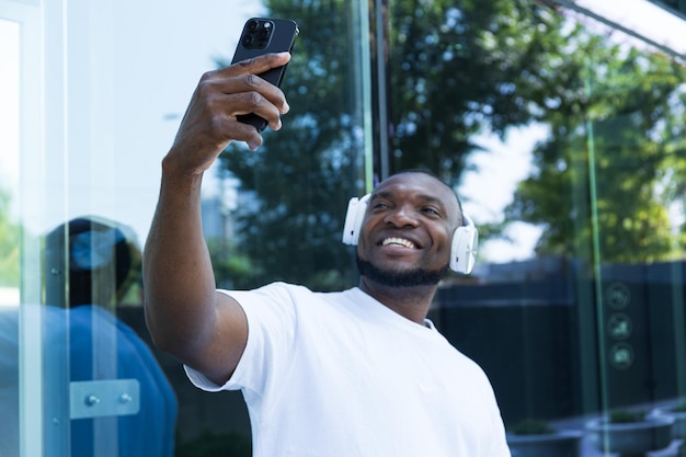 Joven afroamericano elegante escuchando música en auriculares con un teléfono inteligente en las manos