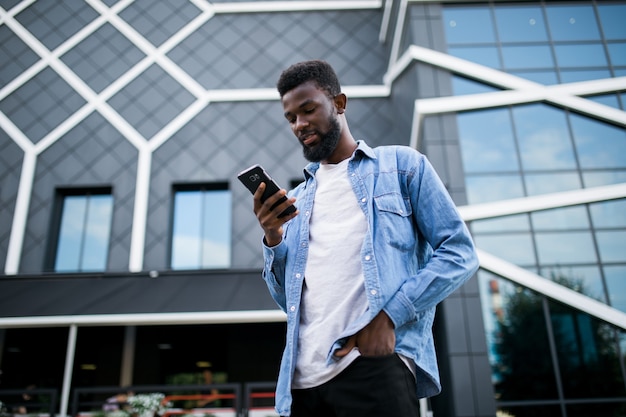 Foto joven afroamericano enviando mensajes de texto celular caminando en la ciudad