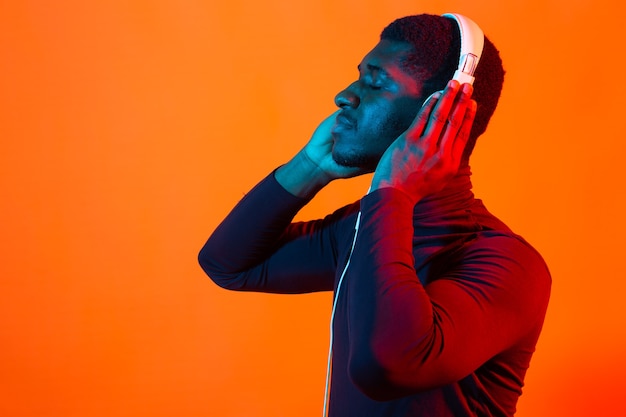 Joven afroamericano escuchando música en auriculares con luz de neón con espacio de copia. Masculino