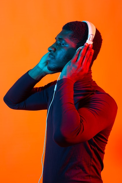 Joven afroamericano escuchando música en auriculares con luz de neón. Retrato masculino. Concepto