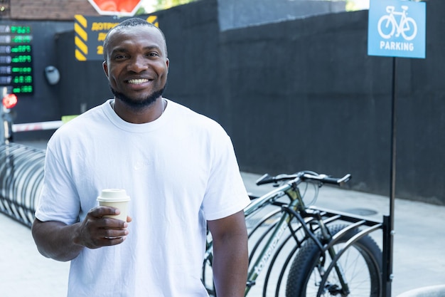 Un joven afroamericano con estilo con un café en la mano en un estacionamiento de bicicletas