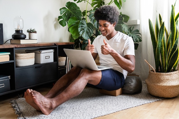 Joven afroamericano hace gestos Thumbs up sign durante una videollamada usando laptop. En concepto de casa. Concepto de tecnología.