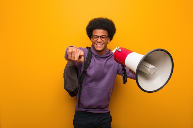 Joven afroamericano holdinga un megáfono alegre y sonriente apuntando al frente