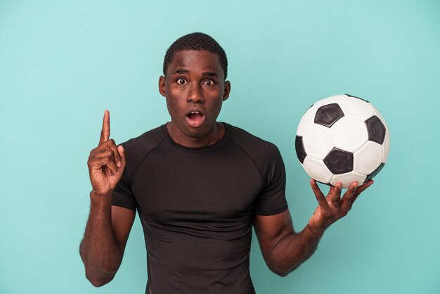 Joven afroamericano jugando al fútbol aislado de fondo azul con un concepto de inspiración de ideas