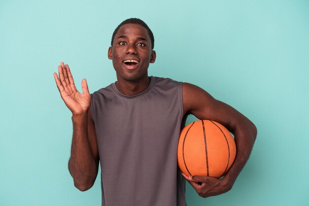 Joven afroamericano jugando baloncesto aislado de fondo azul sorprendido y conmocionado