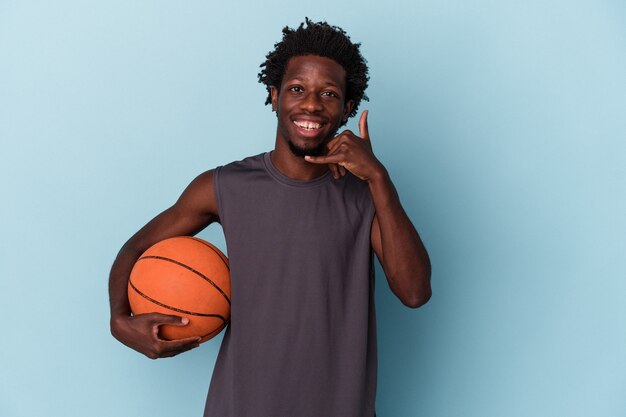 Joven afroamericano jugando baloncesto aislado sobre fondo azul mostrando un gesto de llamada de teléfono móvil con los dedos.