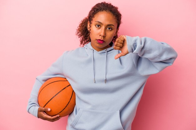 Joven afroamericano jugando baloncesto aislado sobre fondo rosa mostrando un gesto de aversión, pulgares hacia abajo. Concepto de desacuerdo.