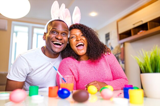 Joven afroamericano y mujer Gente auténtica con lindas orejas de conejo de pascua y pintando huevos en la casa