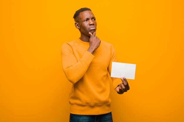 Joven afroamericano negro contra la pared naranja abriendo una pancarta