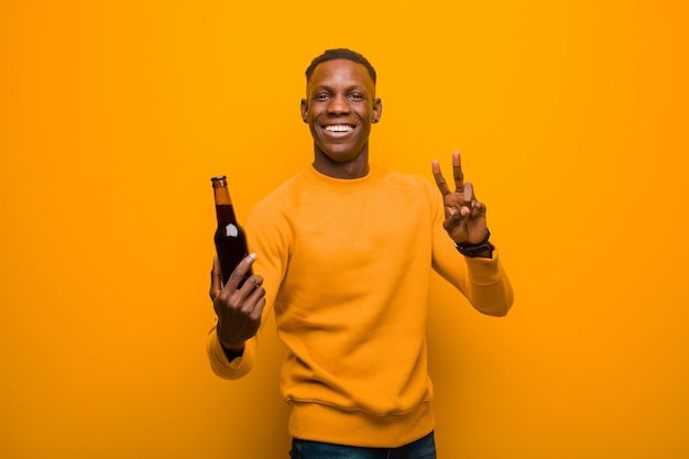 Joven afroamericano negro contra la pared de naranja con una cerveza