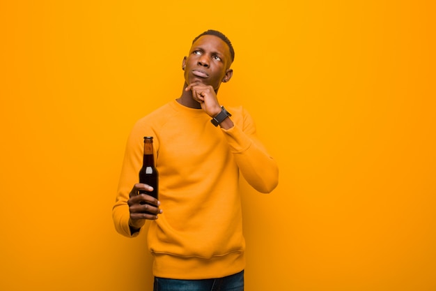 Joven afroamericano negro contra la pared de naranja con una cerveza