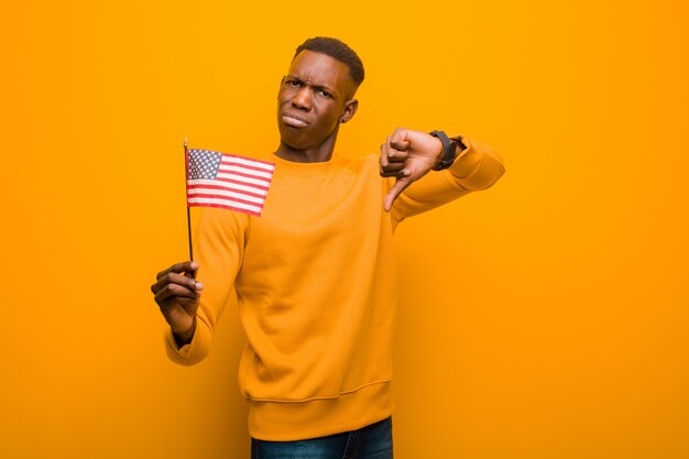 Joven afroamericano negro contra la pared naranja sosteniendo una bandera de Estados Unidos