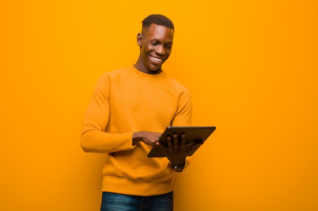 Joven afroamericano negro contra la pared naranja con una tableta inteligente