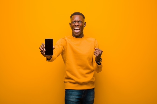 Joven afroamericano negro contra la pared naranja con un teléfono inteligente