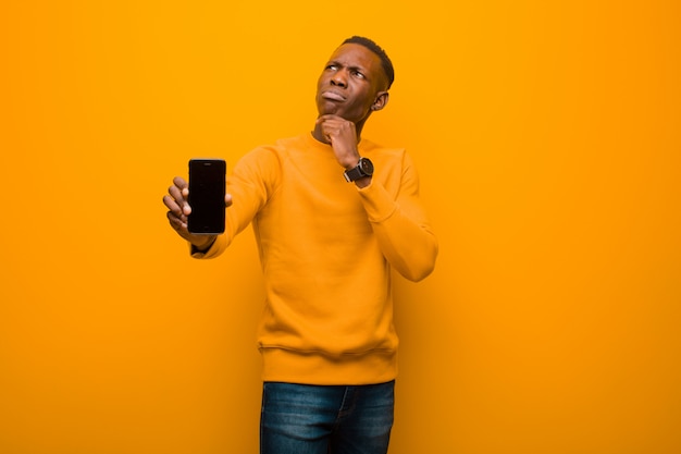 Joven afroamericano negro contra la pared naranja con un teléfono inteligente