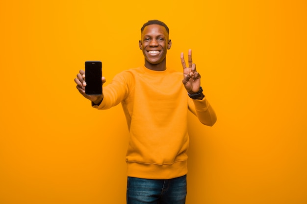 Joven afroamericano negro contra la pared naranja con un teléfono inteligente