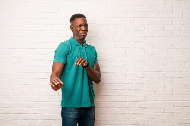 Joven afroamericano negro se siente asqueado y con náuseas, retrocediendo de algo desagradable, maloliente o apestoso, diciendo asco contra la pared de ladrillo