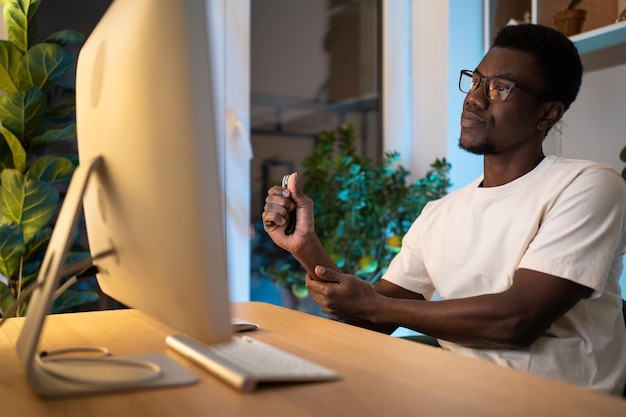 Un joven afroamericano se ocupa de la muñeca de la mano usando un expansor durante un largo tiempo de trabajo en la computadora