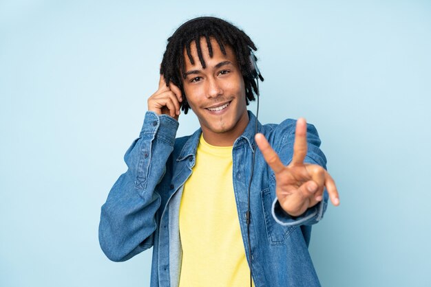 Joven afroamericano en la pared azul escuchando música y cantando