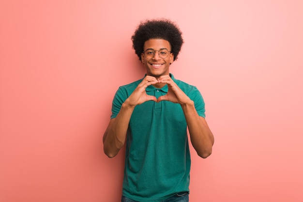 Joven afroamericano en una pared rosada haciendo una forma de corazón con las manos