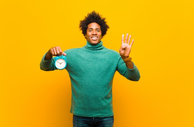 Joven afroamericano con un reloj de alarma contra naranja