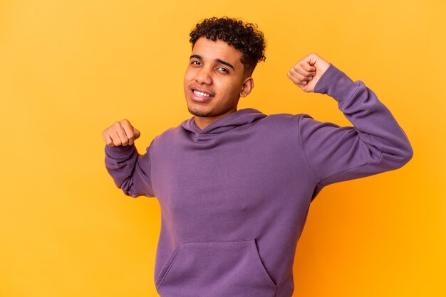 Joven afroamericano rizado aislado en morado celebrando un día especial, salta y levanta los brazos con energía.