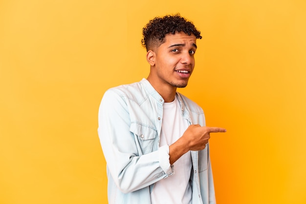 Joven afroamericano rizado aislado en púrpura sonriendo y apuntando a un lado, mostrando algo en el espacio en blanco.