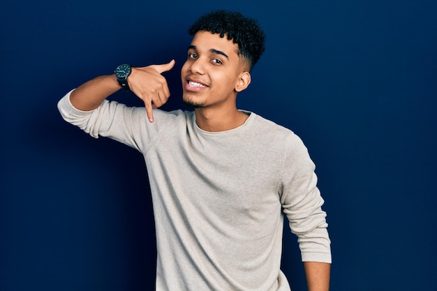 Joven afroamericano con ropa informal sonriendo haciendo gestos telefónicos con la mano y los dedos como hablar por teléfono. comunicar conceptos.