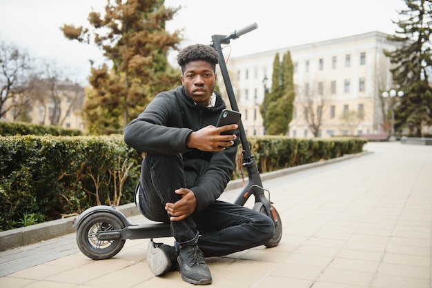 Joven afroamericano con scooter eléctrico en la ciudad